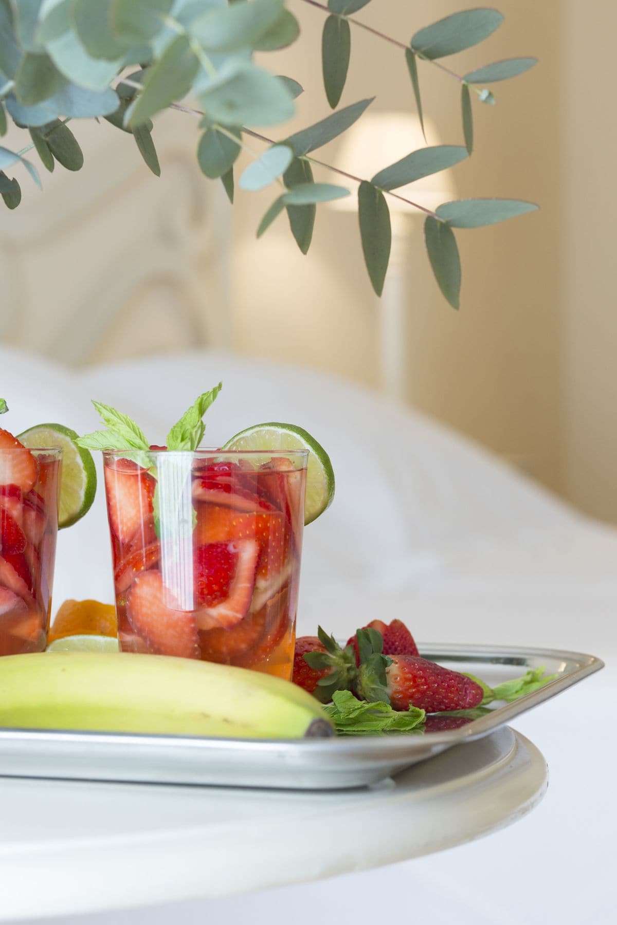 A tray with three glasses of fruit drink, a banana, and strawberries on a white table.