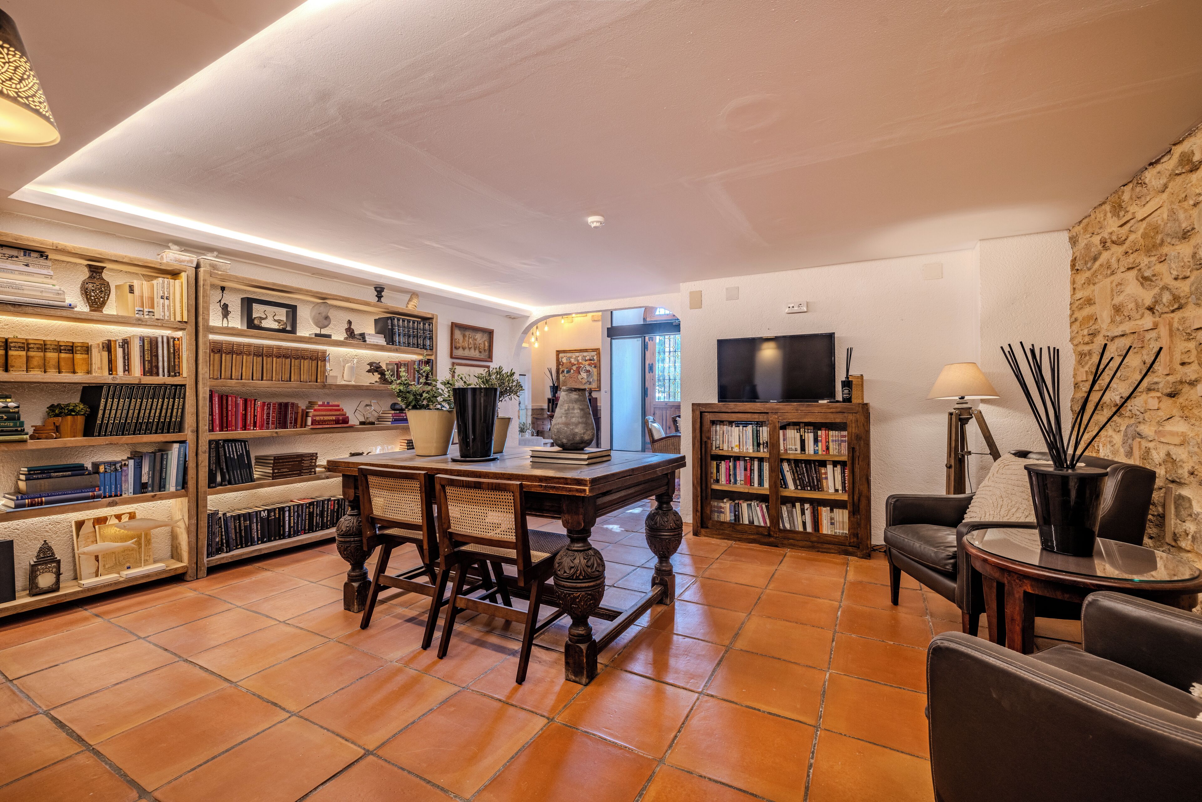 Un salon chaleureux avec une table en bois, des chaises, des étagères, un téléviseur et un mur en pierre.