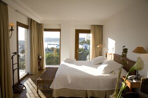 A hotel room with a large bed, a view of the city, and a balcony with a wicker chair.