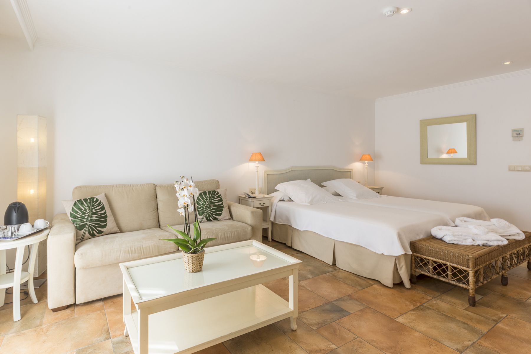 A hotel room with a bed, a sofa, a small table, and a nightstand.