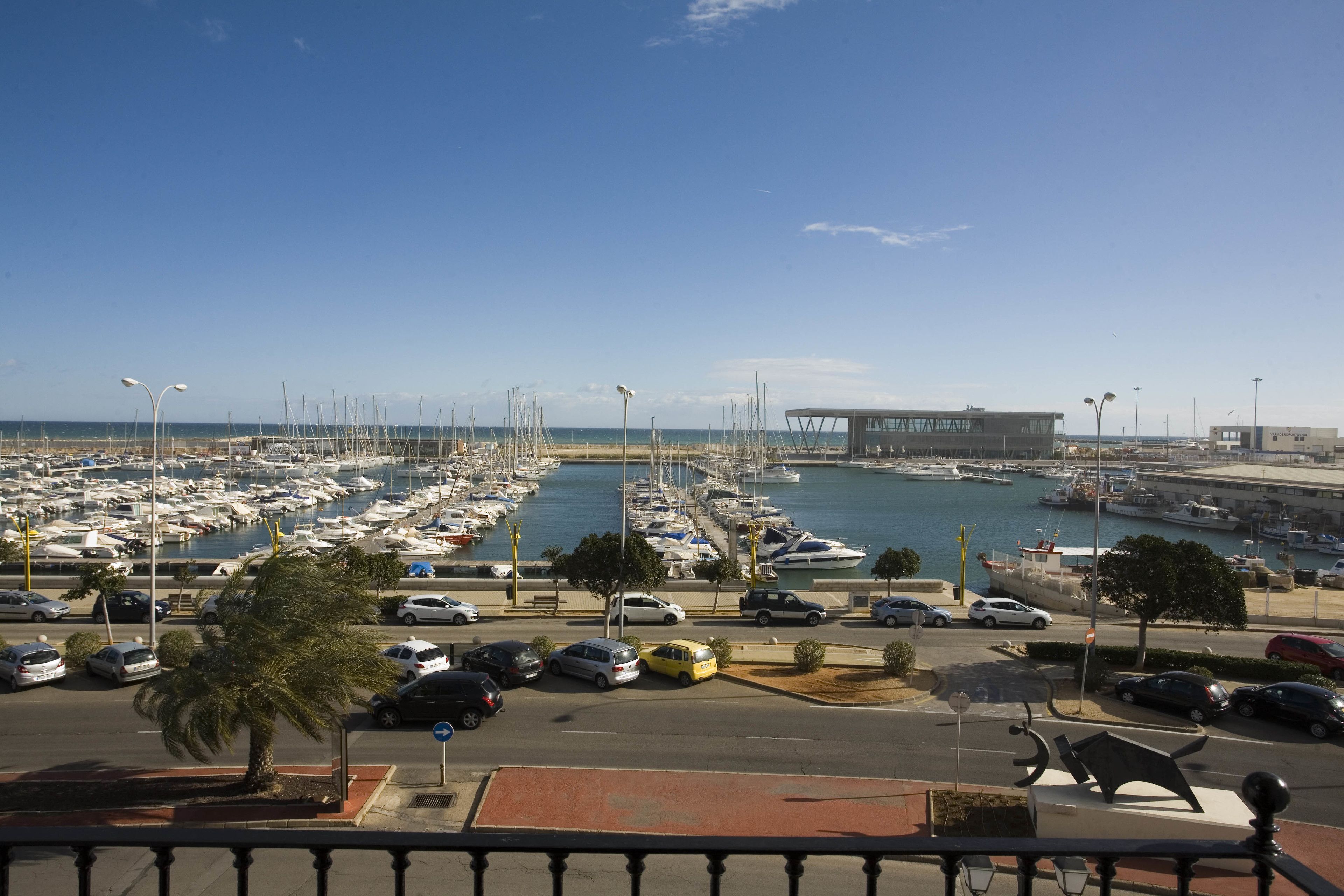 A marina with numerous boats docked, a parking area with cars, and a building in the background.
