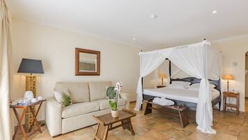 A hotel room with a four-poster bed, a sofa, a small table, and a bedside table with lamps.