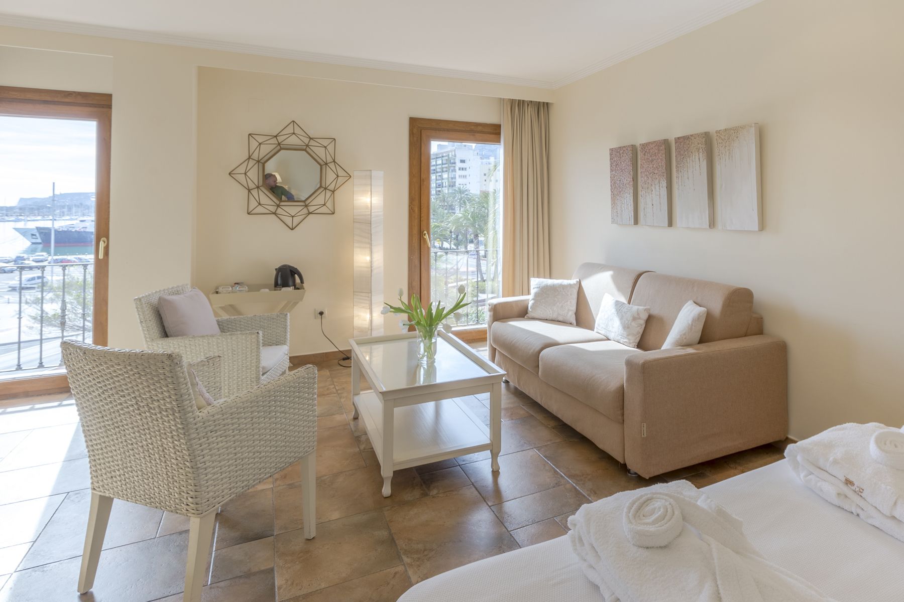 Un salón moderno con un sofá, un sillón, una mesa de centro y vistas de la ciudad a través de amplias ventanas.