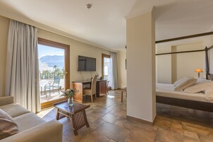A hotel room with a bed, a desk, a chair, a TV, and a view of mountains.