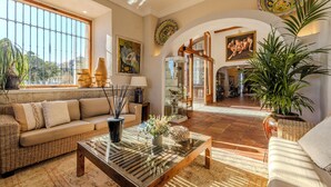 A spacious living room with a large window, a sofa, a coffee table, and a dining area with a glass partition. - La Posada del Mar Hotel (Denia)