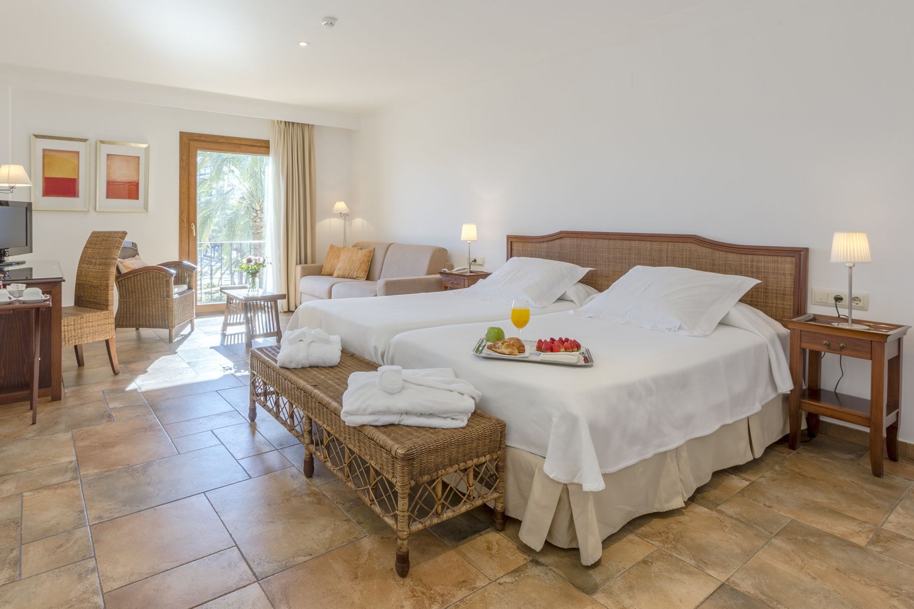 A hotel room with two beds, a sitting area with a sofa and chairs, a dining table, and a TV.