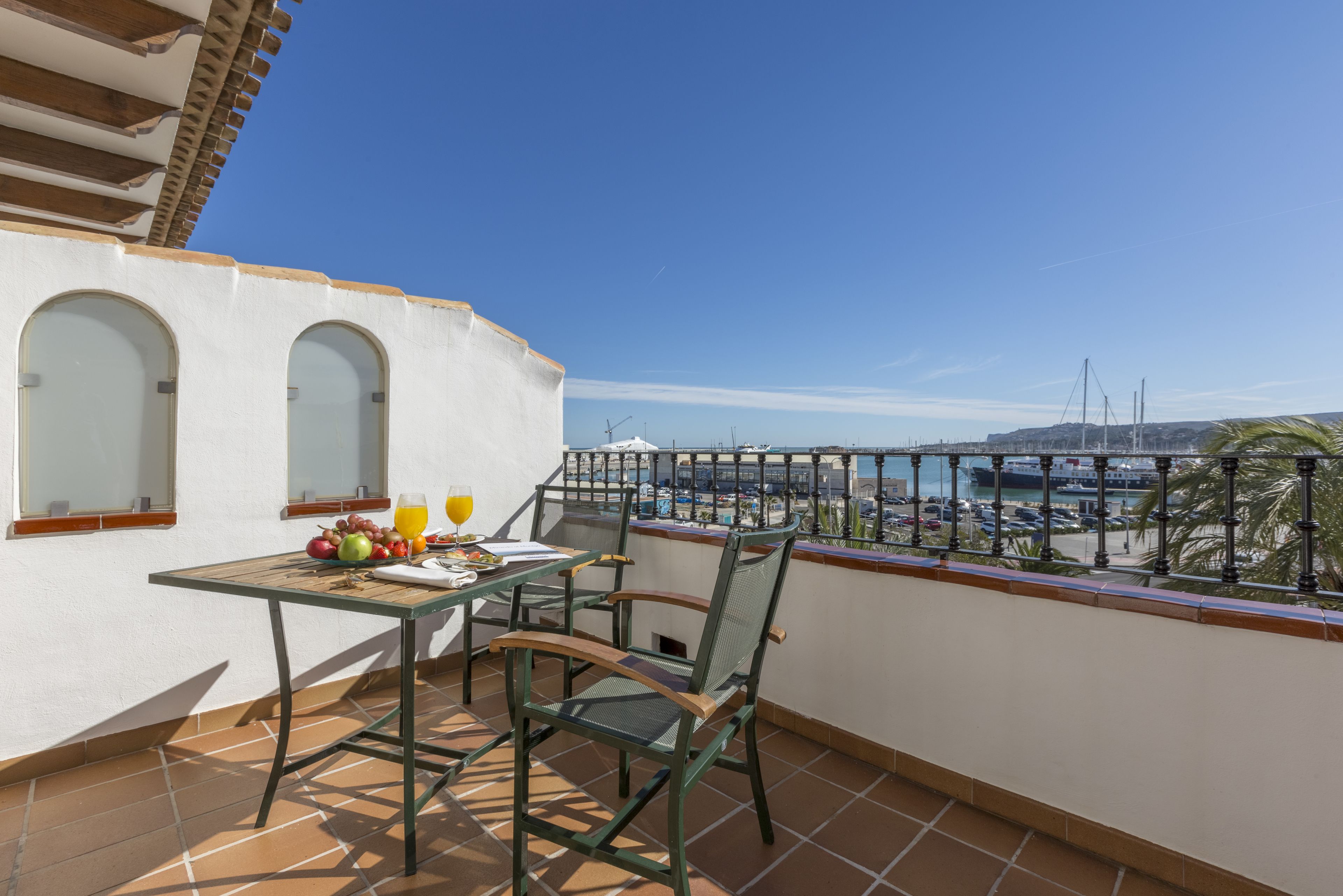 Un balcón con mesa, sillas y vista al mar y barcos.
