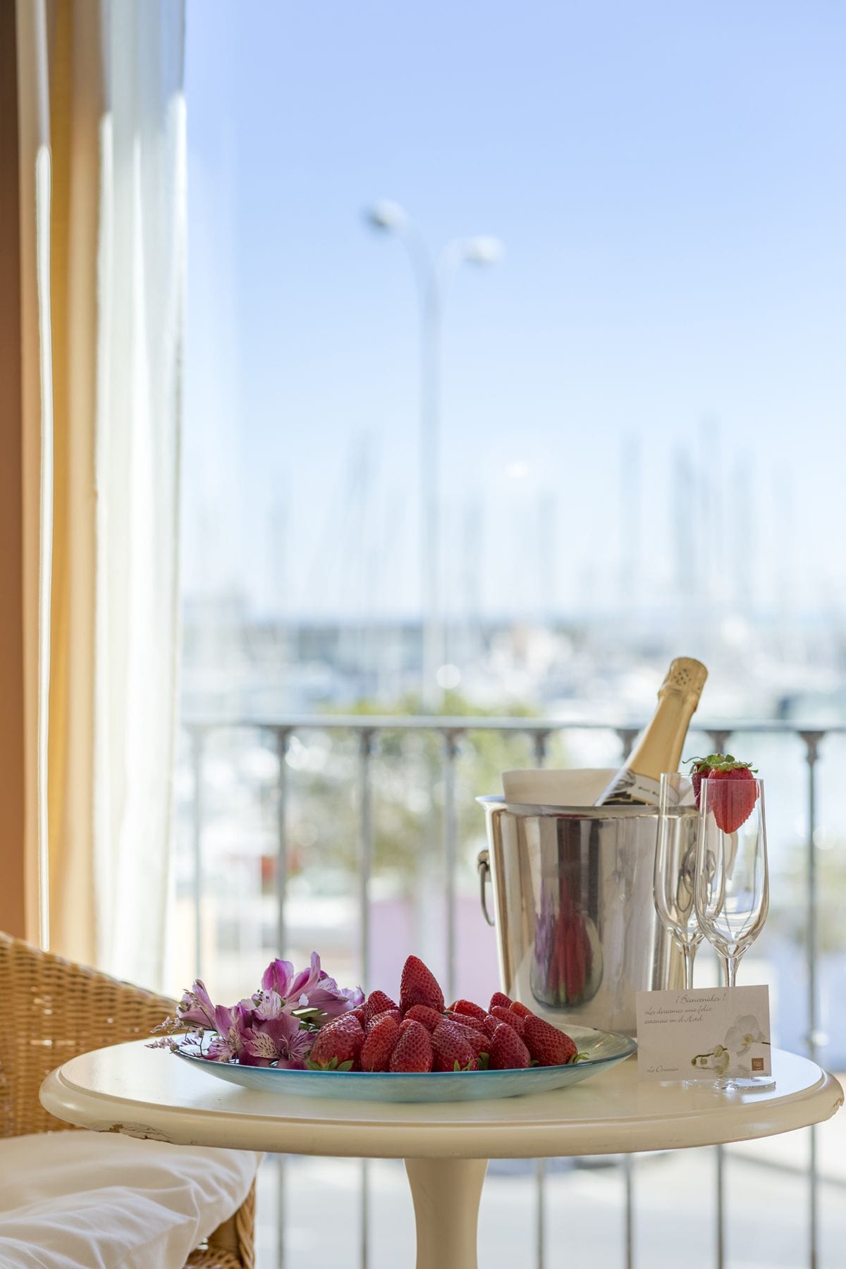 Una mesa con una botella de champán, una jarra y copas en un balcón con vistas a un puerto deportivo.