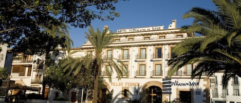 A hotel with a classic facade, arched entrances, and palm trees in the foreground.