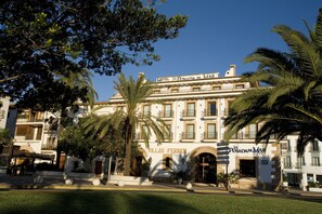 A hotel with a classic facade, arched entrances, and palm trees in the foreground.