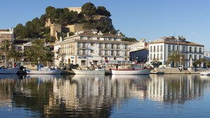 A waterfront hotel with multiple stories, a prominent hill in the background, and several boats docked in the water. - La Posada del Mar Hotel (Denia)