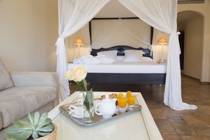 A bedroom with a bed, canopy, bedside lamps, a tray with breakfast items, and a potted plant.