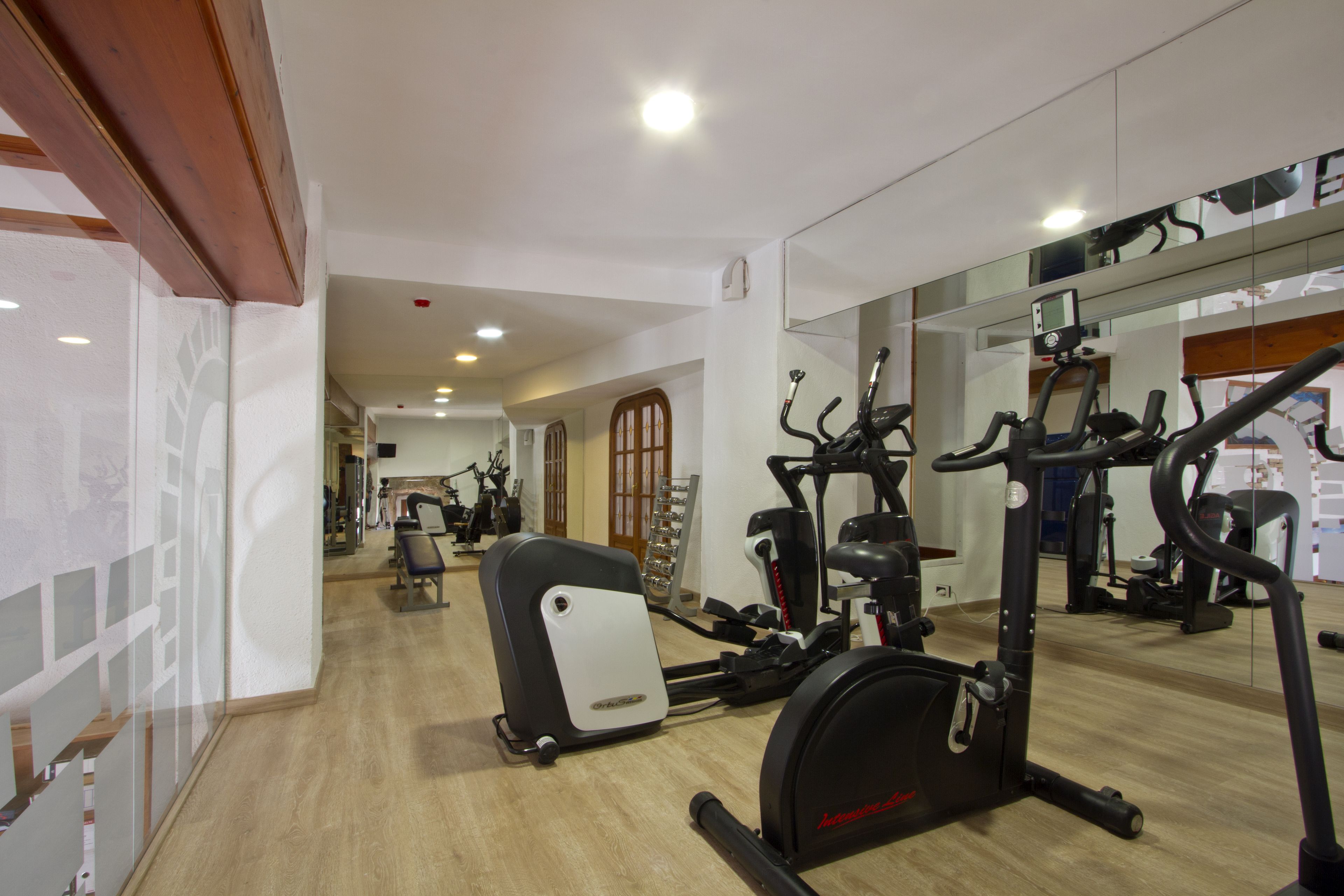 A gym with exercise equipment, wooden flooring, and a large mirror reflecting the space.