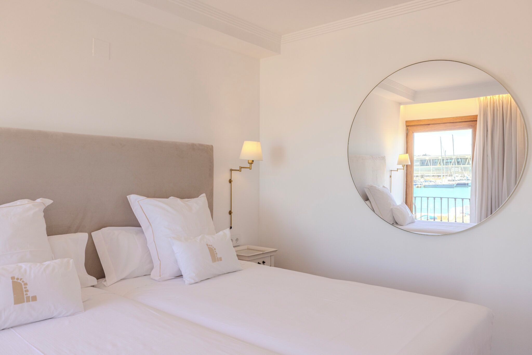 Een hotelkamer met een groot bed, een ronde spiegel en uitzicht op een balkon.