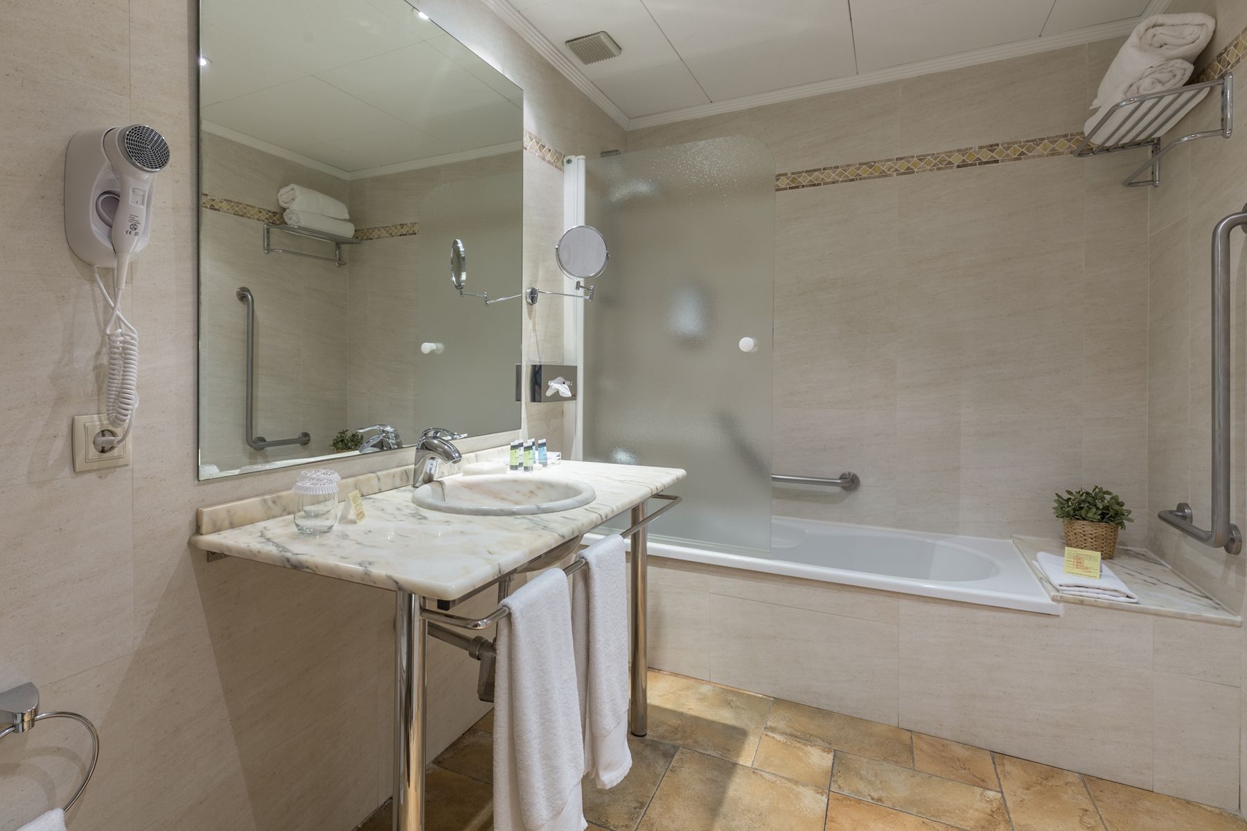 Une salle de bain moderne avec un lavabo en marbre, un sèche-cheveux portatif, une douche à l’italienne et une baignoire.