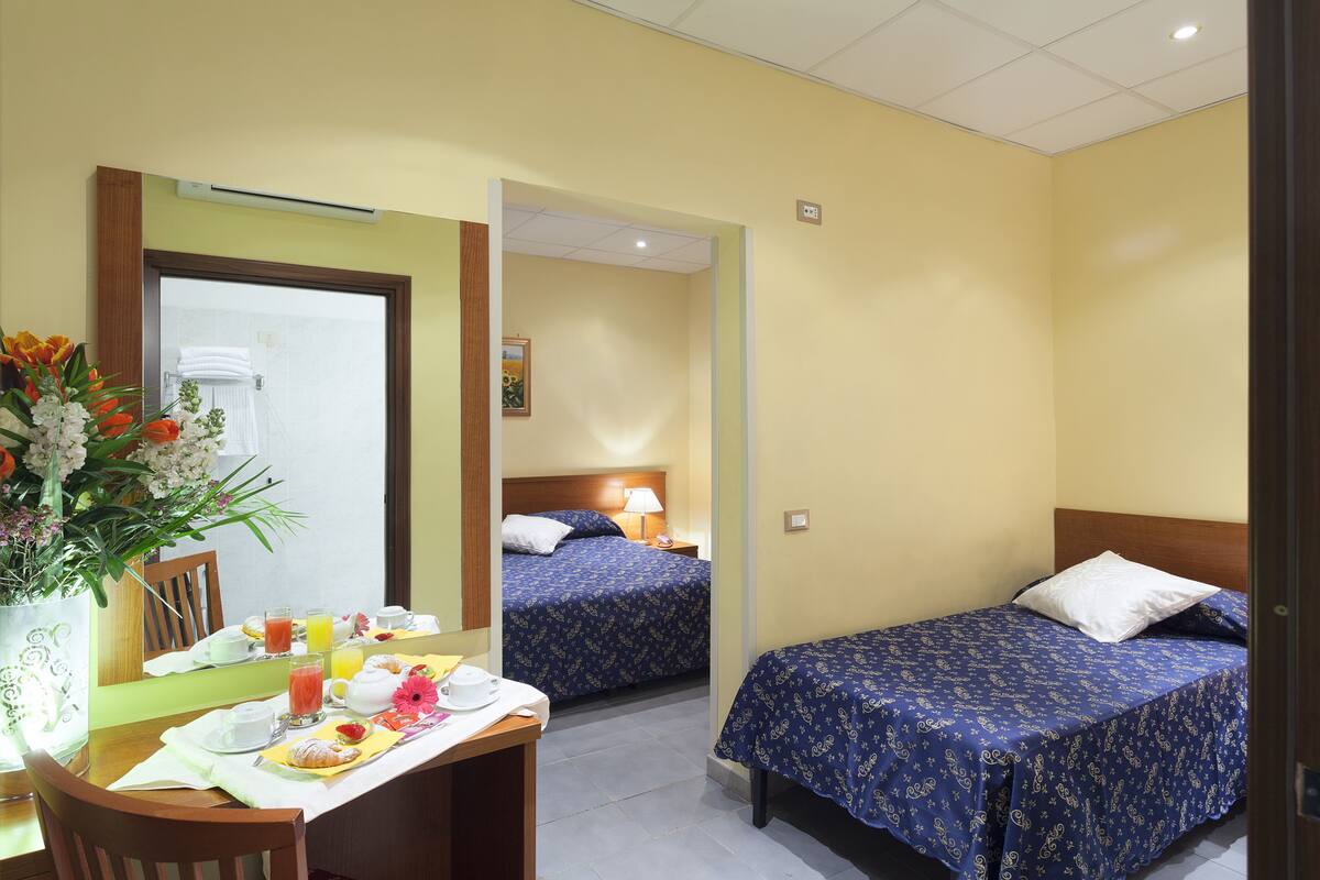 A hotel room with two beds, a dining area with breakfast, and a bathroom visible through an open door.