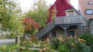 A building with a wooden staircase, a stone wall, and a garden with roses. - Landhotel Schwarzes Ross (Steinsfeld)