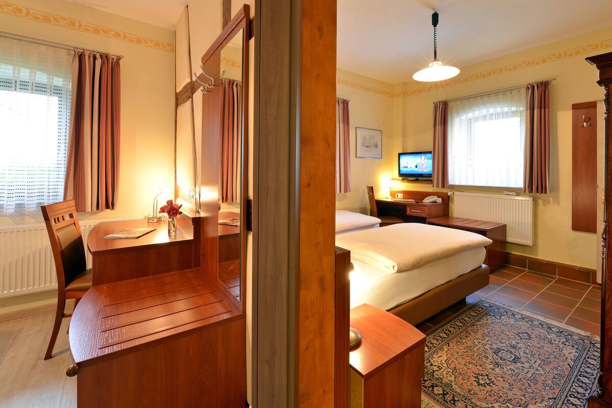 Una habitación de hotel con una cama, un escritorio con silla, un televisor y una ventana con cortinas.