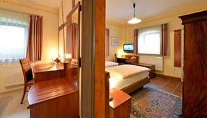 Una habitación de hotel con una cama, un escritorio con silla, un televisor y una ventana con cortinas.
