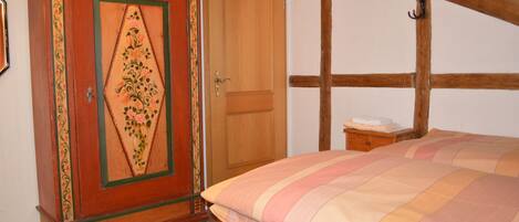 A bedroom with a bed, wooden wardrobe, and a nightstand.