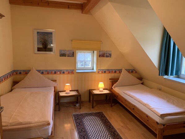 Un acogedor dormitorio en el ático con dos camas individuales, una ventana pequeña y un borde decorativo en la pared.