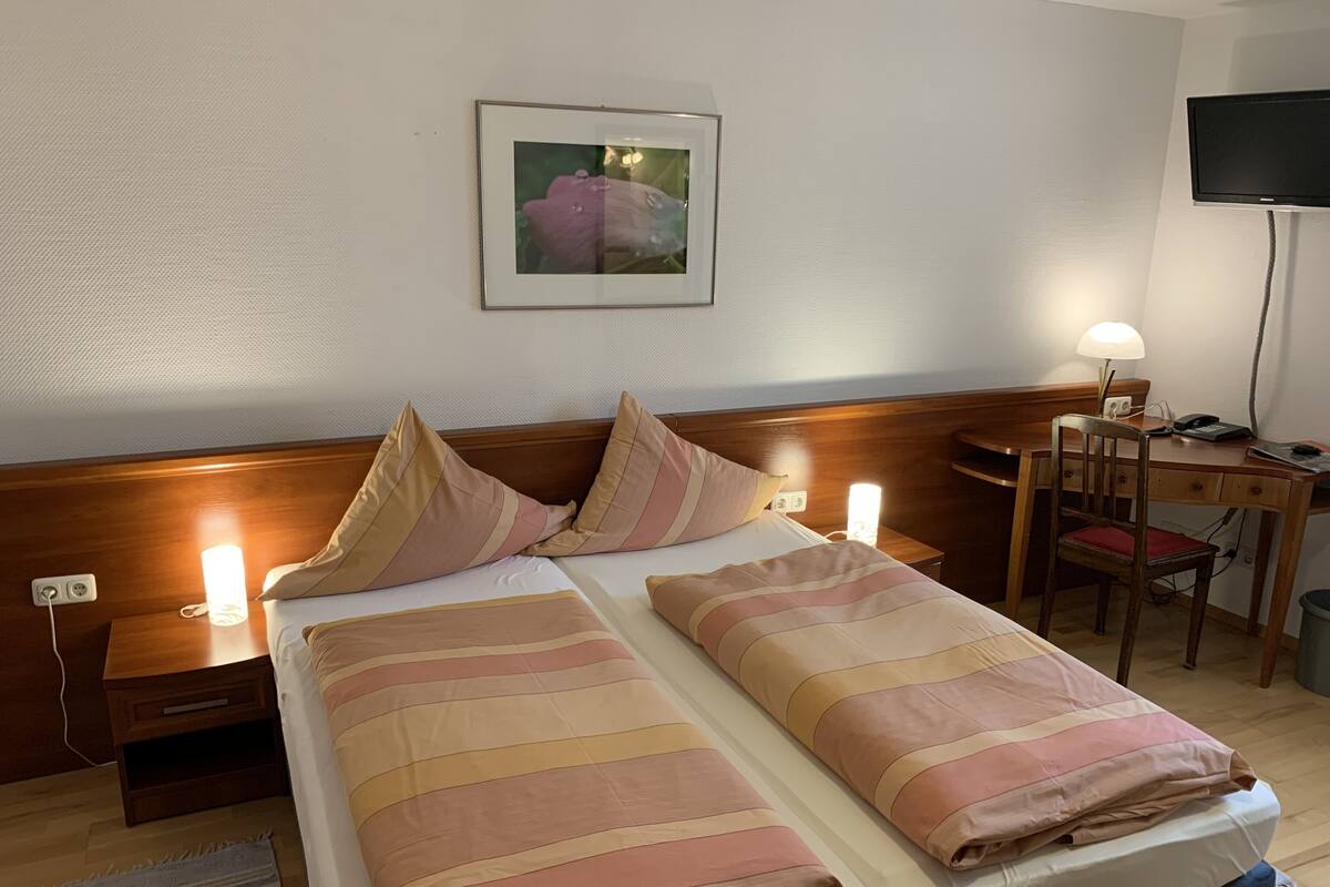 Una habitación de hotel con una cama, lámparas de noche, un escritorio y una silla.