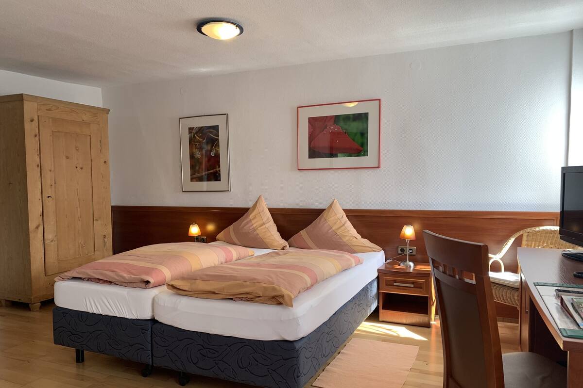 Un cuarto de hotel ordenado con cama, mesitas de noche, televisor y armario de madera.