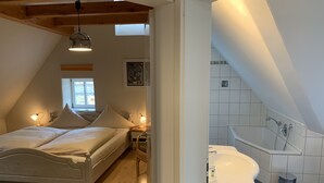 A bedroom with a bed, bedside lamps, and a window. There is a bathroom with a bathtub and a sink. - Landhotel Schwarzes Ross (Steinsfeld)