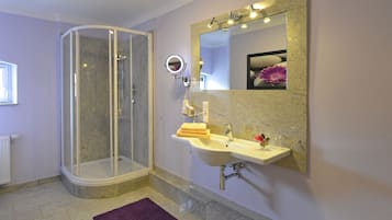 Un baño con ducha de mampara de vidrio, lavamanos con espejo y una alfombra de baño morada.