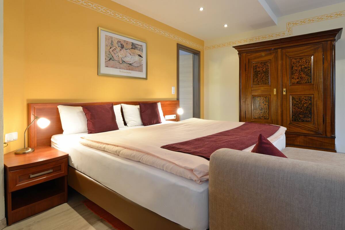 Habitación de hotel con una cama grande, una mesita de noche con lámpara, un armario de madera y un cuadro enmarcado en la pared.