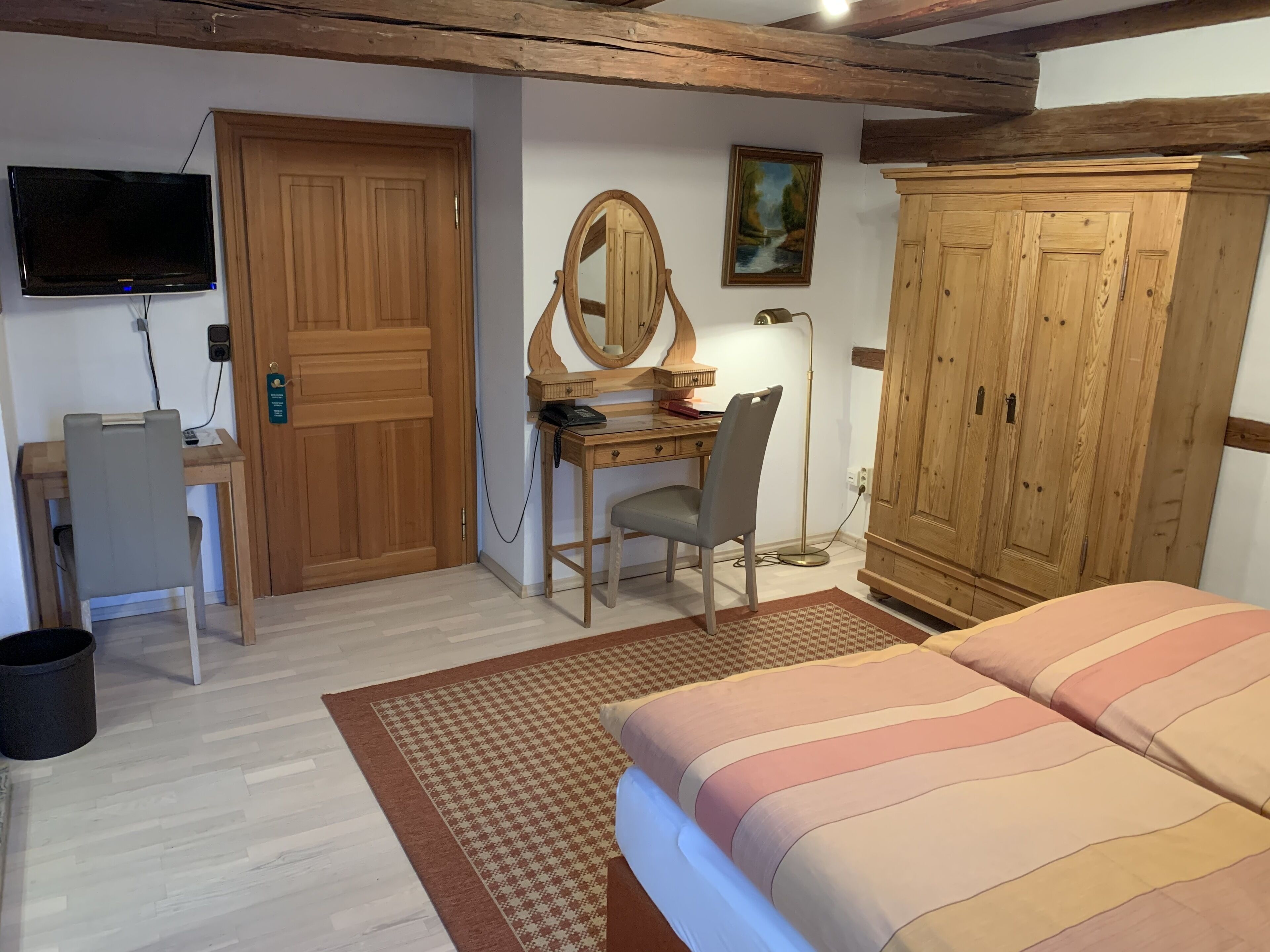 Un dormitorio con cama, escritorio con silla, armario, televisor y un cuadro en la pared.