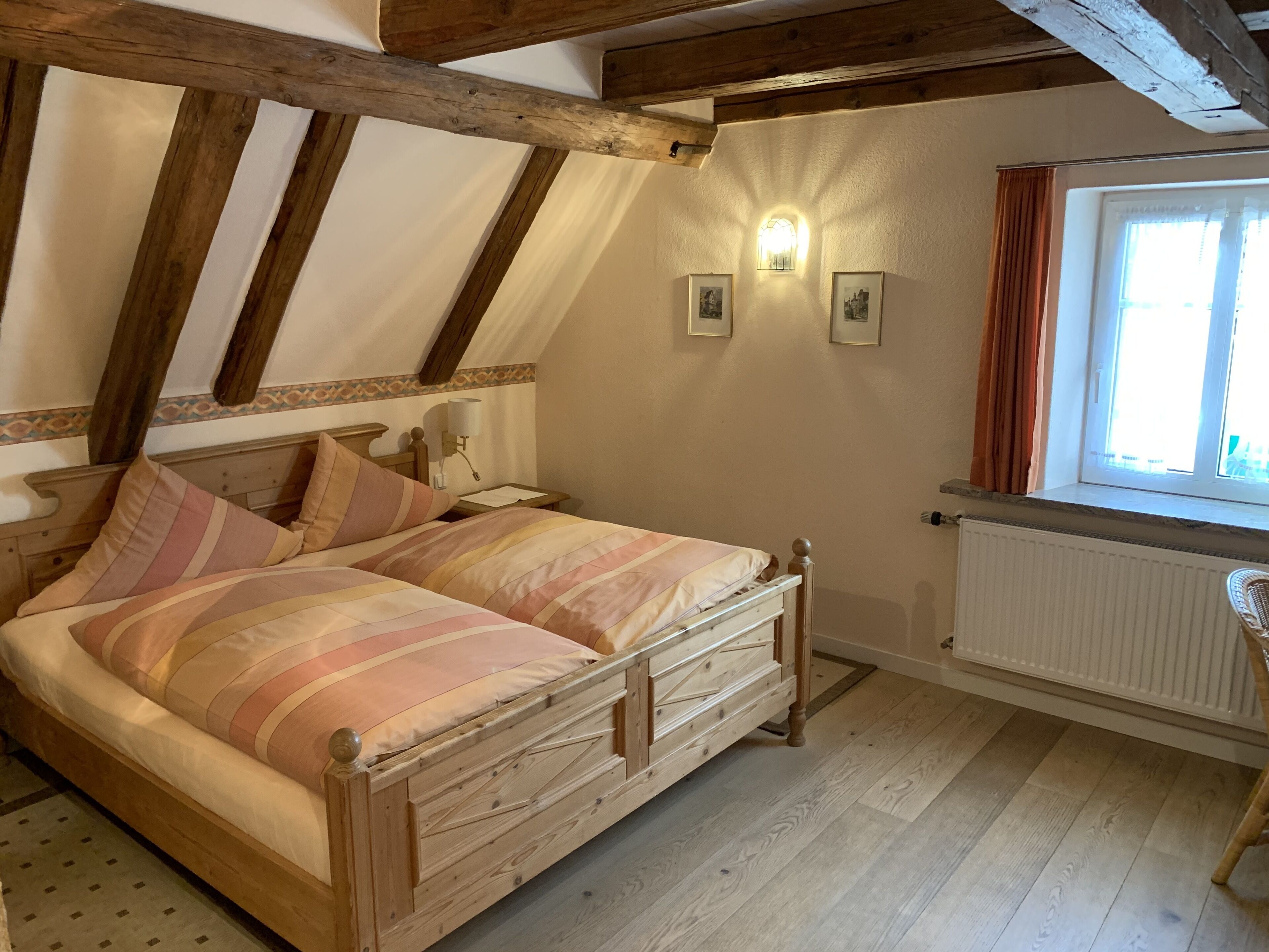 Une chambre à coucher avec un lit en bois, une table de chevet, une lampe fixée au mur et une fenêtre avec des rideaux.