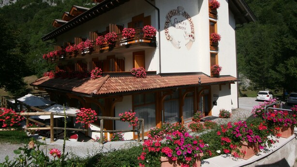 A two-story building with a white facade, wooden balconies, and red flowers. - Hotel Garni Lago Nembia (San Lorenzo Dorsino)