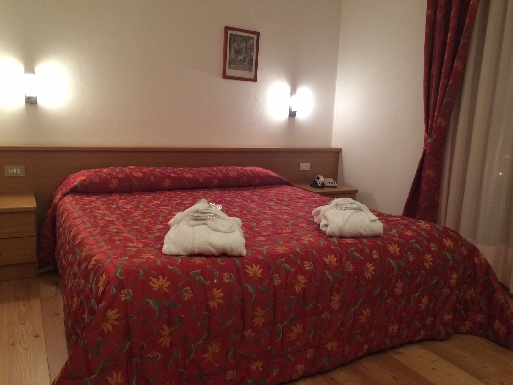 A hotel room with a bed, a bedside table, a phone, and a wall-mounted light fixture.