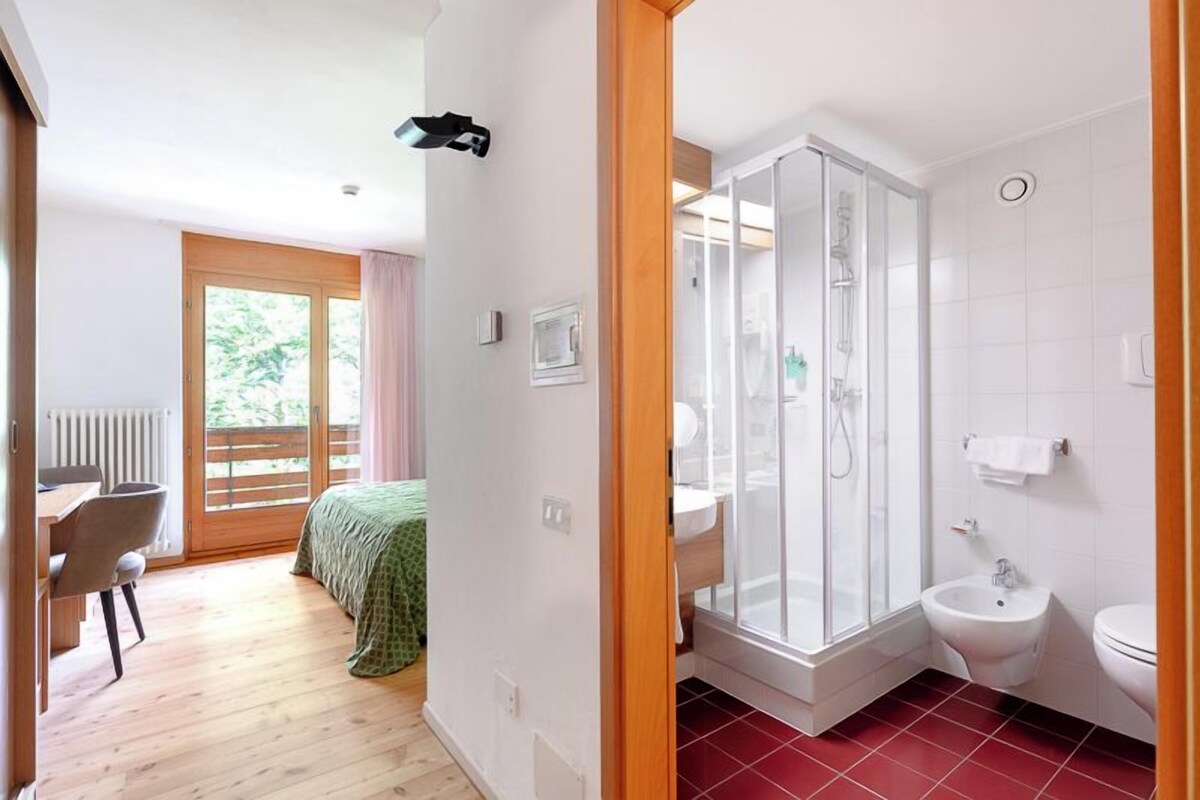 A bedroom with a bed, a desk, and a chair. There is a bathroom with a shower, sink, and toilet.