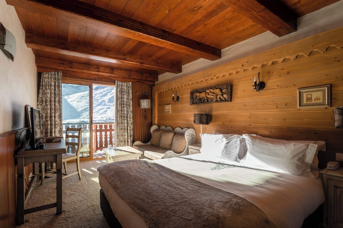 A cozy room with a large bed, wooden ceiling, and a view of mountains through a window.