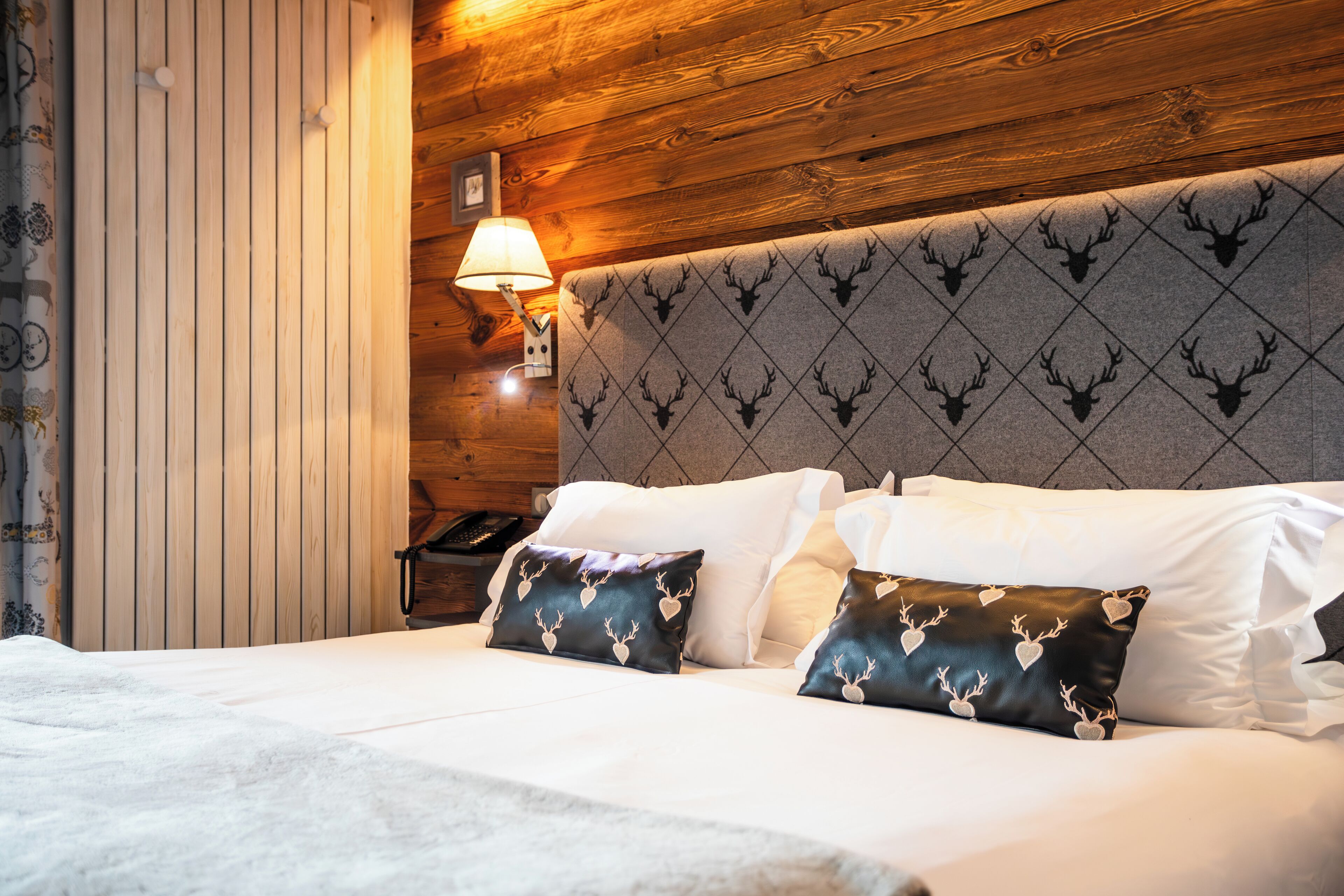 A neatly made bed with white linens and two decorative pillows with deer antlers.