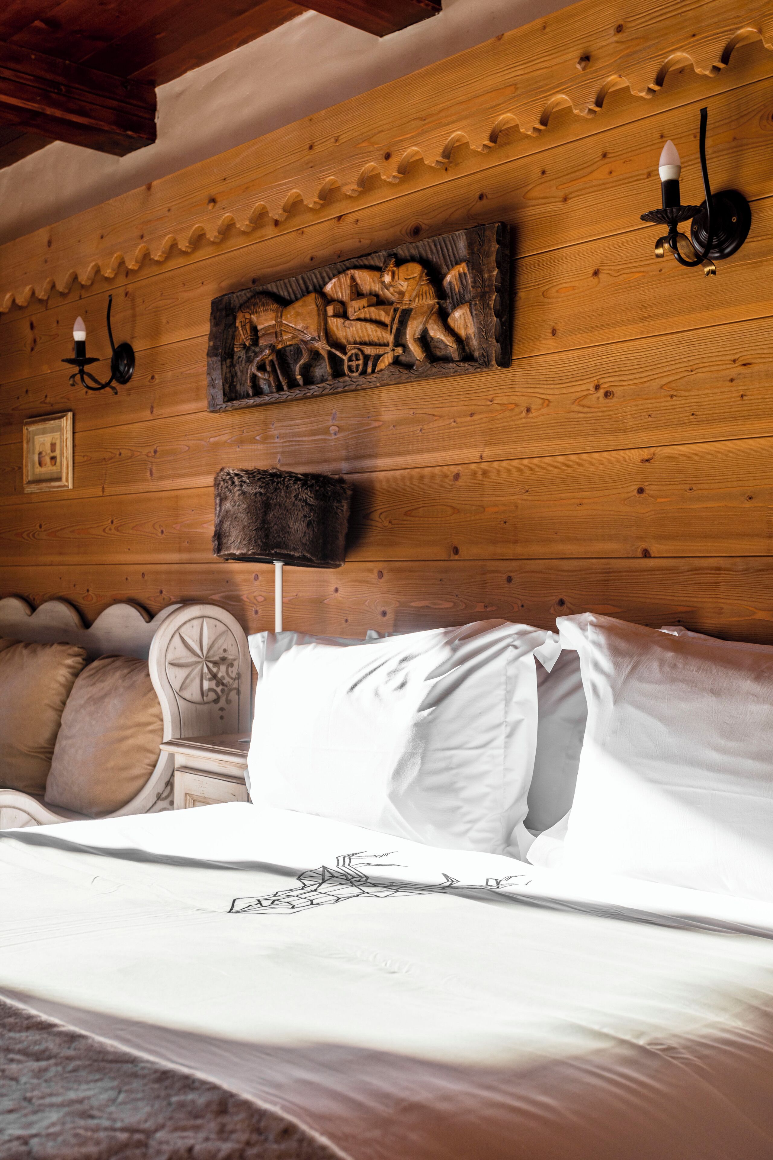 A wooden cabin-style bedroom with a bed, a wall-mounted lamp, and a rustic wall carving.