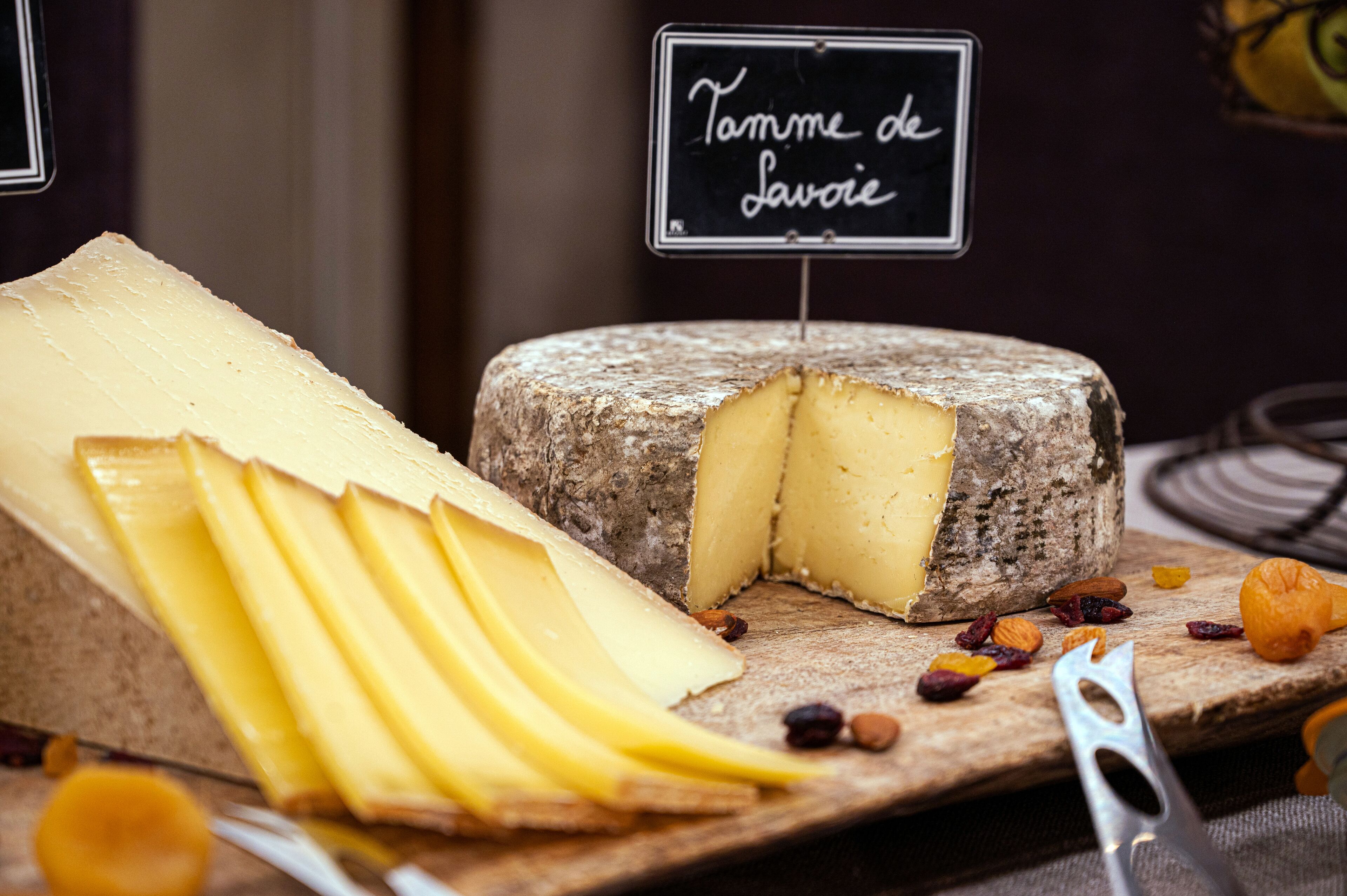 A wheel of cheese with a sign that reads "Tomme de Savoie" and sliced cheese on a wooden board.