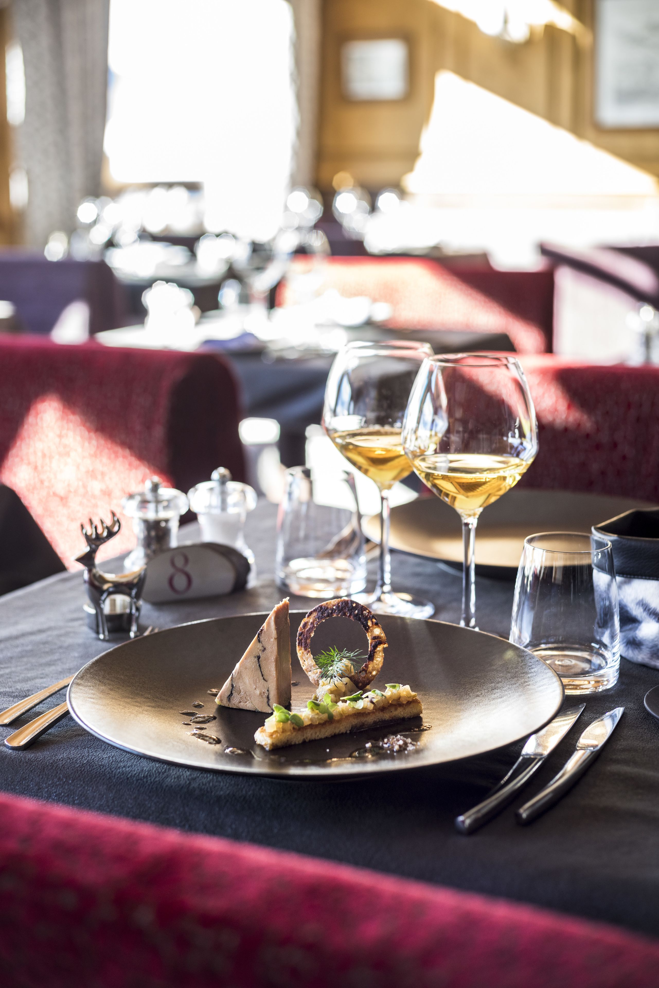 A dining table with a dessert, two wine glasses, and a menu.