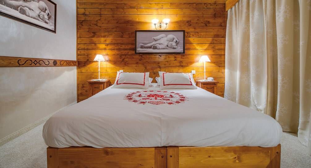 Une chambre à coucher aux murs lambrissés, avec un grand lit, deux lampes de chevet et un tableau encadré accroché au mur.