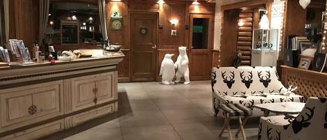 Un espace de vie chaleureux et bien éclairé, agrémenté d’un mur d’accent en bois, d’un coin salon central avec des meubles recouverts de tissus à motifs et d’un comptoir de cuisine où sont disposés divers objets.