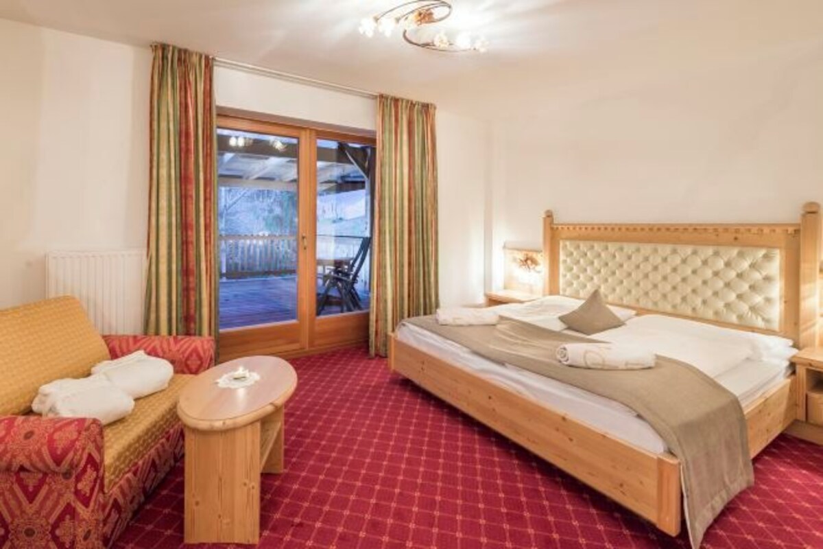 A hotel room with a bed, a sofa, a small table, and a view of the outdoors through a glass door.