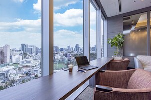 Un espacio de oficina moderno con una computadora portátil, un teléfono inteligente y una taza de café sobre un escritorio, con vistas a un paisaje urbano a través de amplios ventanales.
