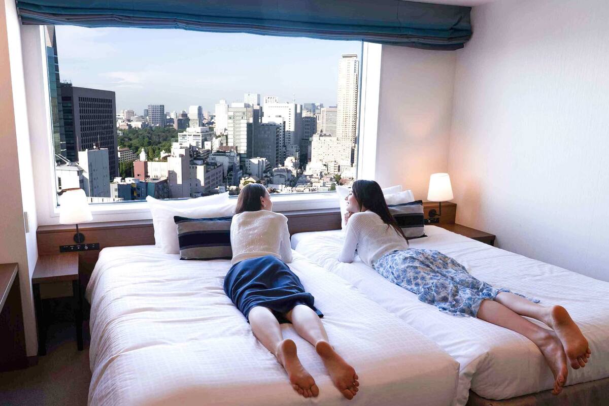 Two beds in a hotel room with a city view.