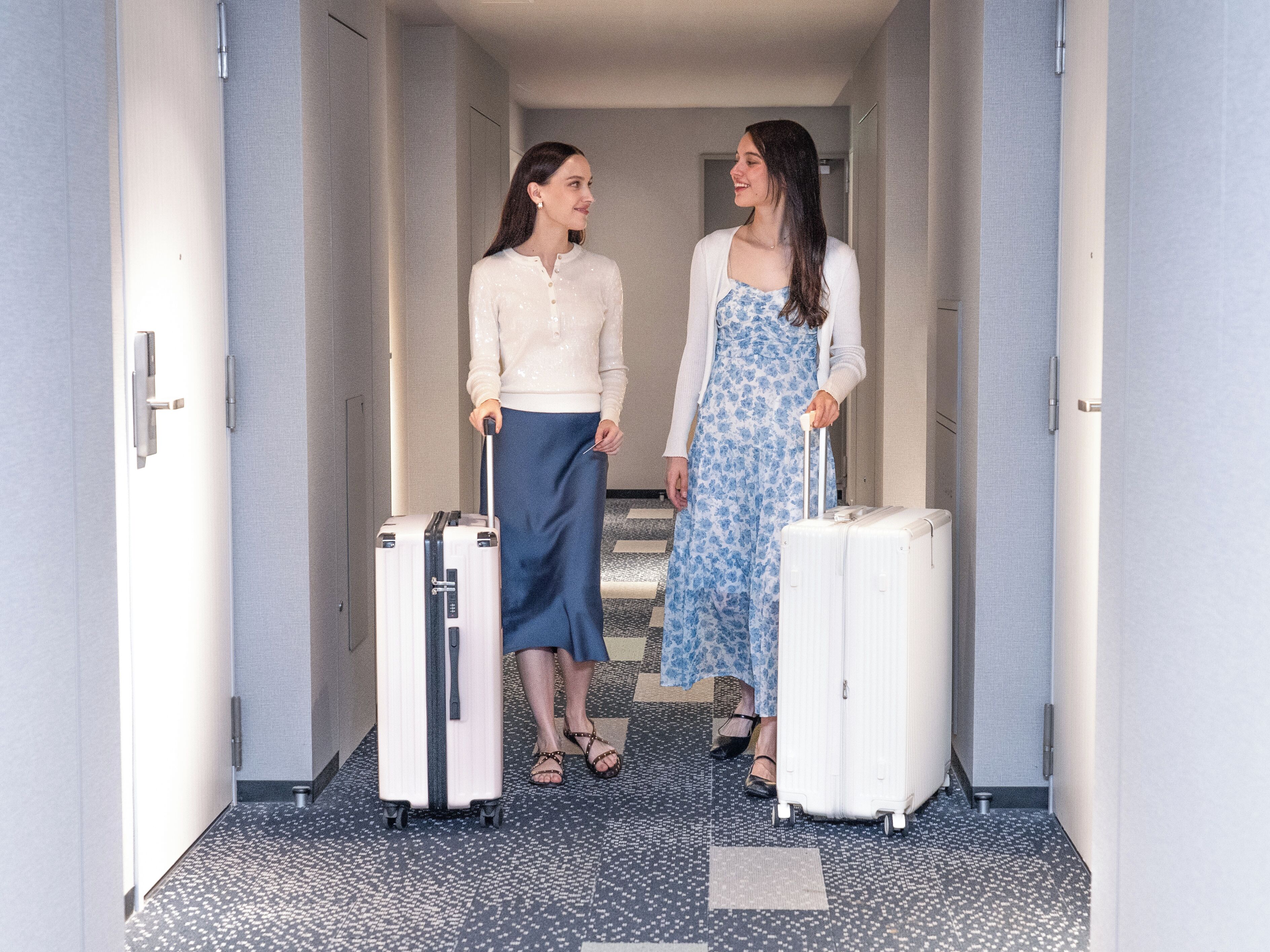 A hallway with two individuals carrying suitcases, suggesting a hotel setting.