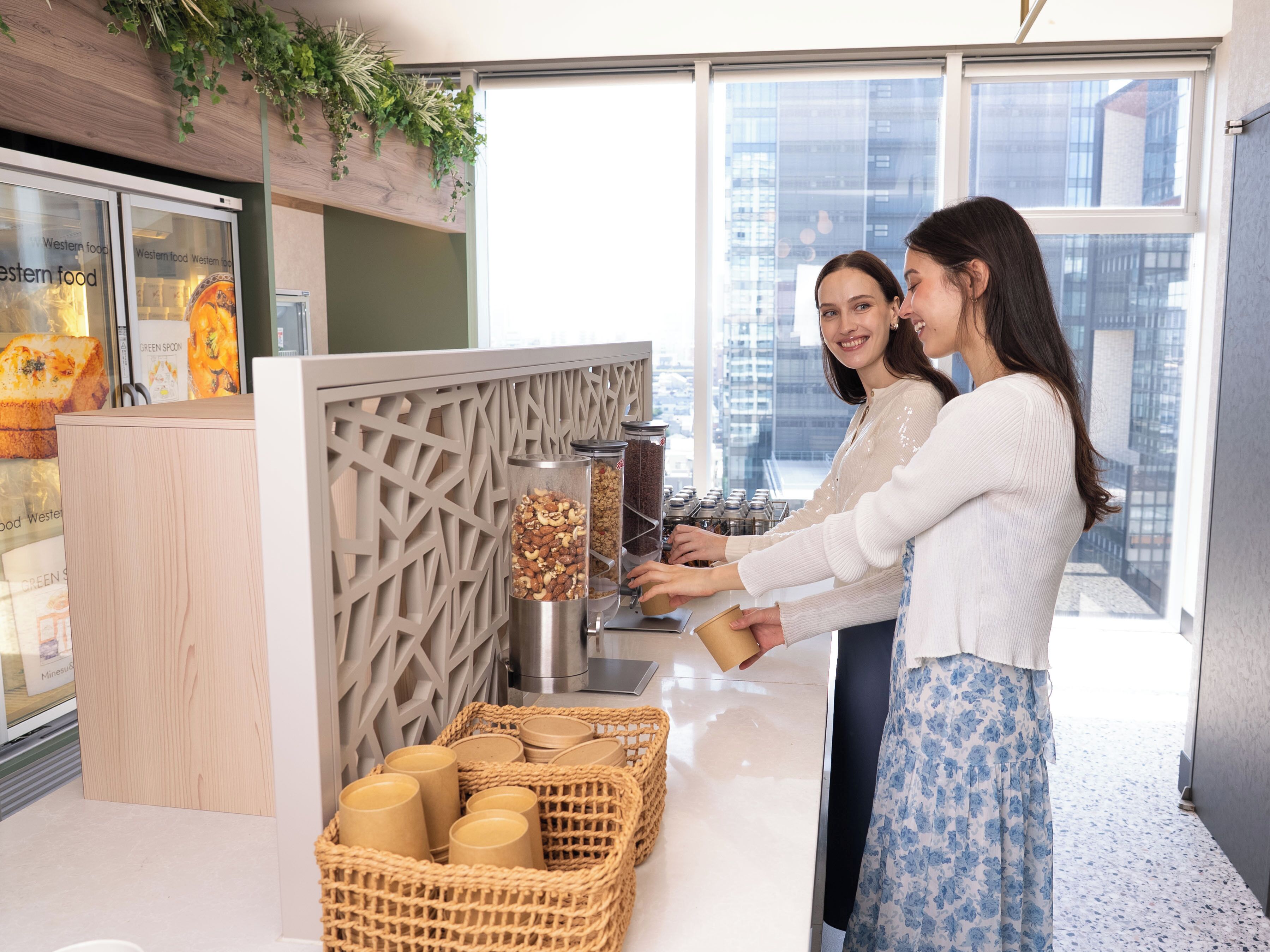 A modern interior with a counter, jars of nuts, and a view of the city through large windows.