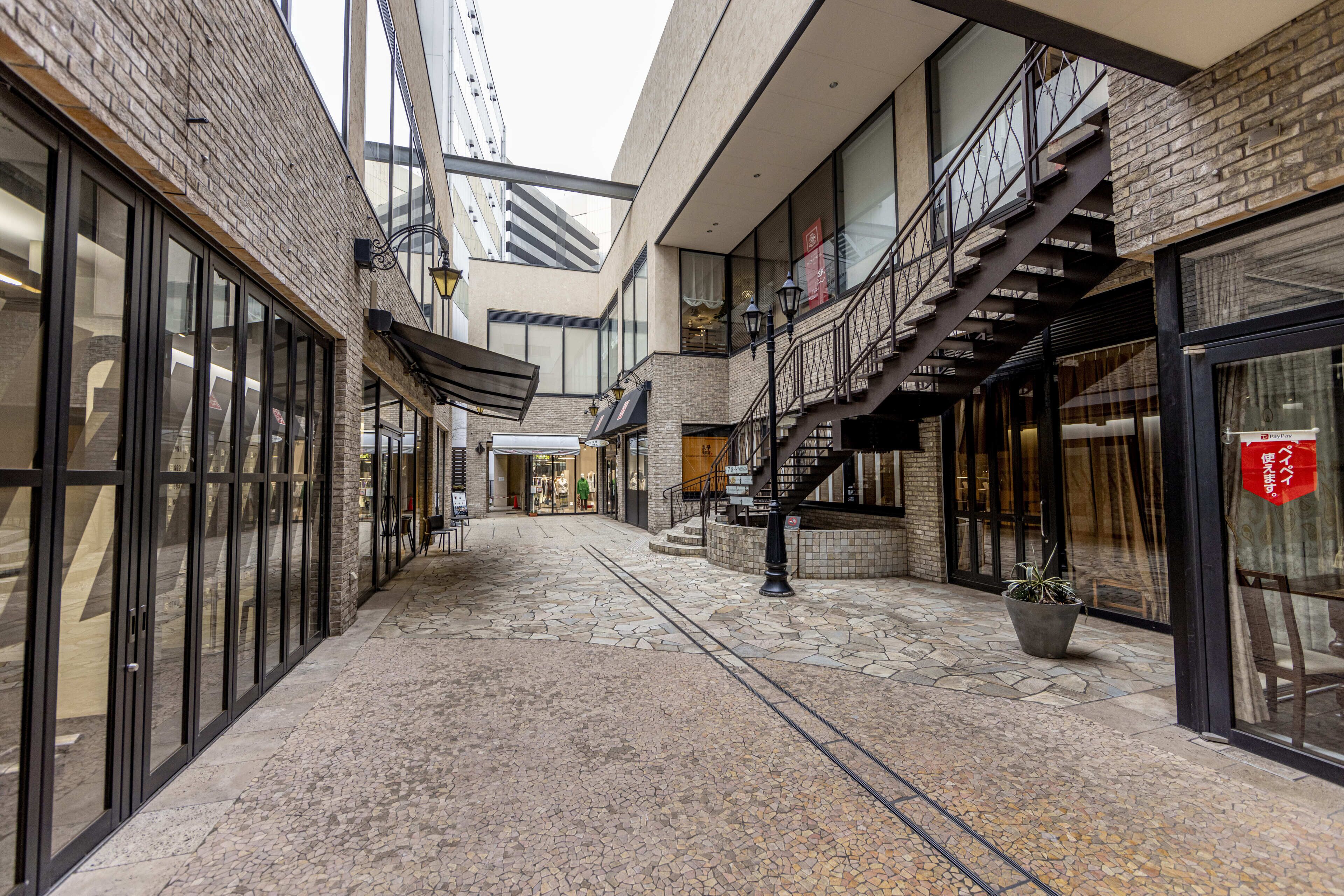 A corridor with a stone floor, a staircase, and glass doors on the left.