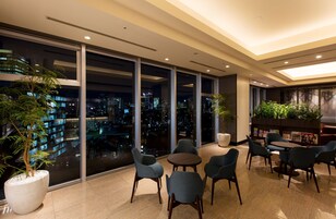 A modern indoor space with large windows offering a nighttime city view, comfortable seating, and indoor plants.
