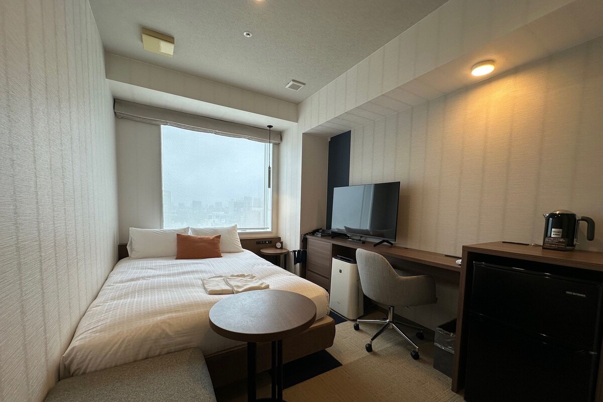 A hotel room with a bed, a desk, a chair, a television, a coffee maker, and a small table.